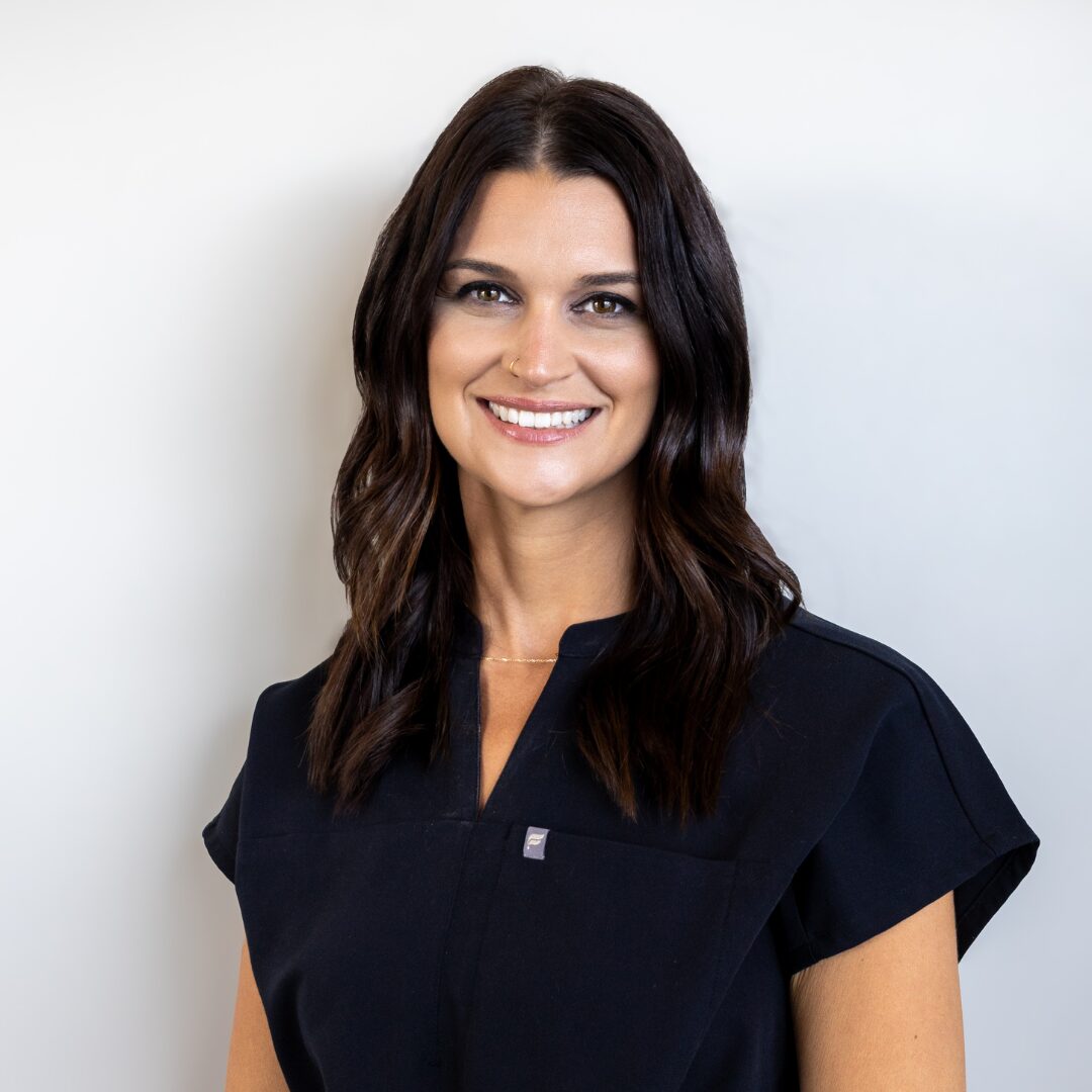 Callie Brickert of Silique Companies smiling in black scrubs with long dark brown hair against a light gray background.