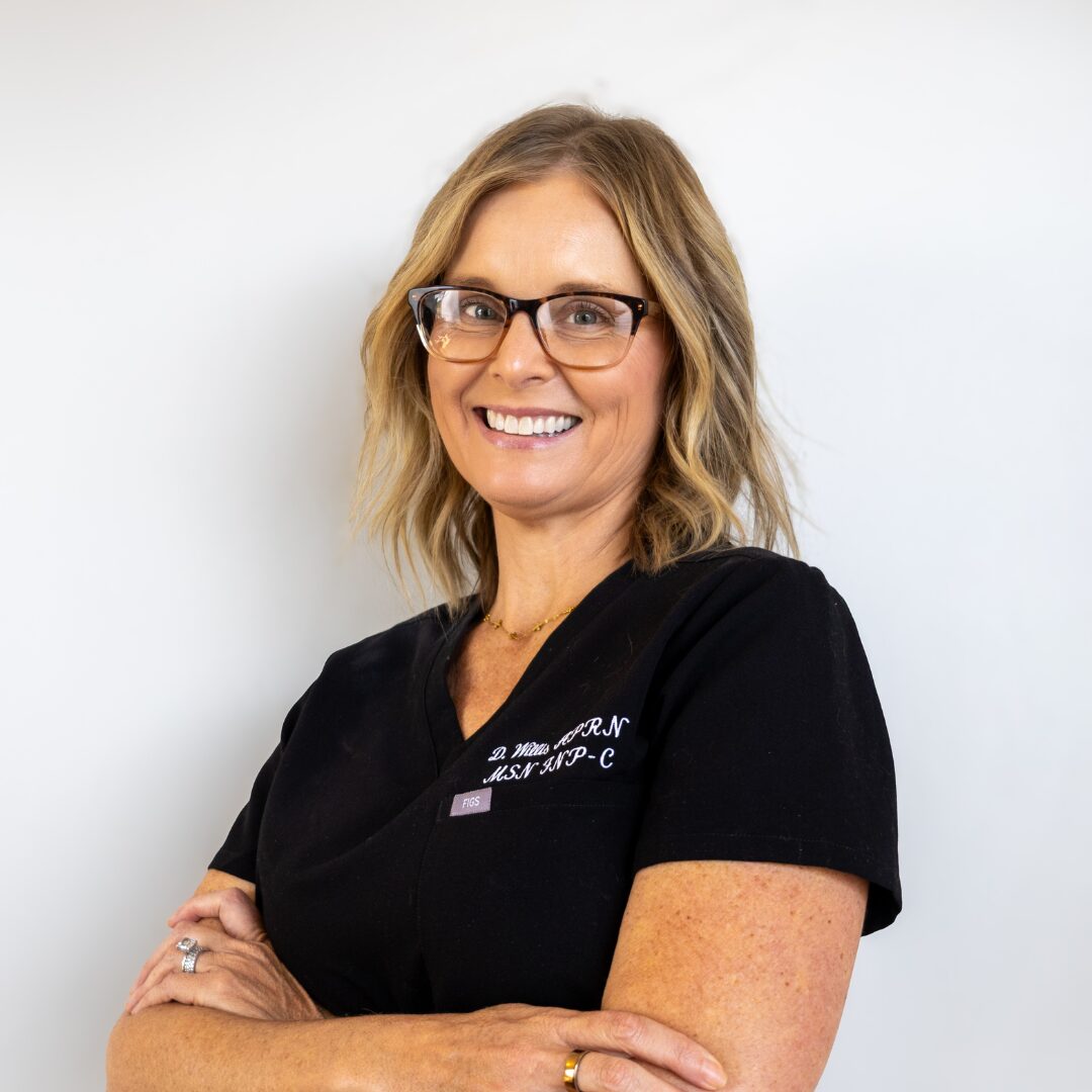 Deonna Willis, APRN, MSN, FNP-C, owner and nurse practitioner at Silique Companies, smiling in black scrubs with arms crossed.